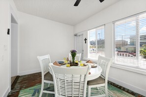 Comedor con una mesa redonda, sillas blancas y una ventana con persianas.