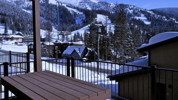 Eine Holzterrasse mit Blick auf einen schneebedeckten Berg und einen Skiort im Hintergrund.