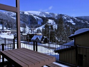 A wooden deck with a view of a snow-covered mountain and a ski resort in the background.