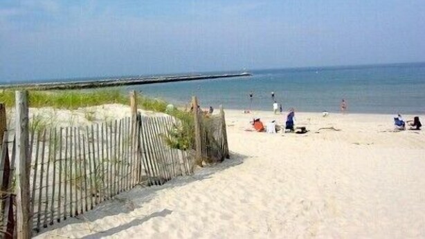 Ein Strand mit einer Holzumzäunung und Personen, die am Ufer entlanggehen.