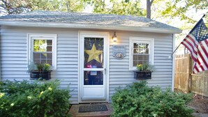 Une maison avec une porte blanche, deux fenêtres, une pancarte indiquant «Bienvenue» et un drapeau américain.