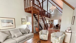 Un vaste salon agrémenté d’un escalier en bois, d’un canapé, de deux fauteuils à motifs et d’un coin repas à l’arrière-plan.