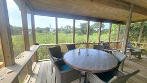 Un espace extérieur abrité, doté d’une table ronde et de chaises en osier, qui offre une vue sur un champ et un bâtiment situé au loin.