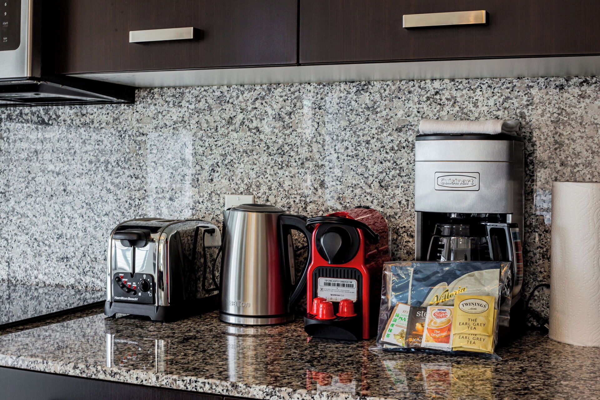 Une cuisine dotée d’un plan de travail en granit, d’un grille-pain de la marque Hamilton Beach, d’une bouilloire électrique rouge, d’une machine à café Cuisinart et de paquets de thé Earl Grey.