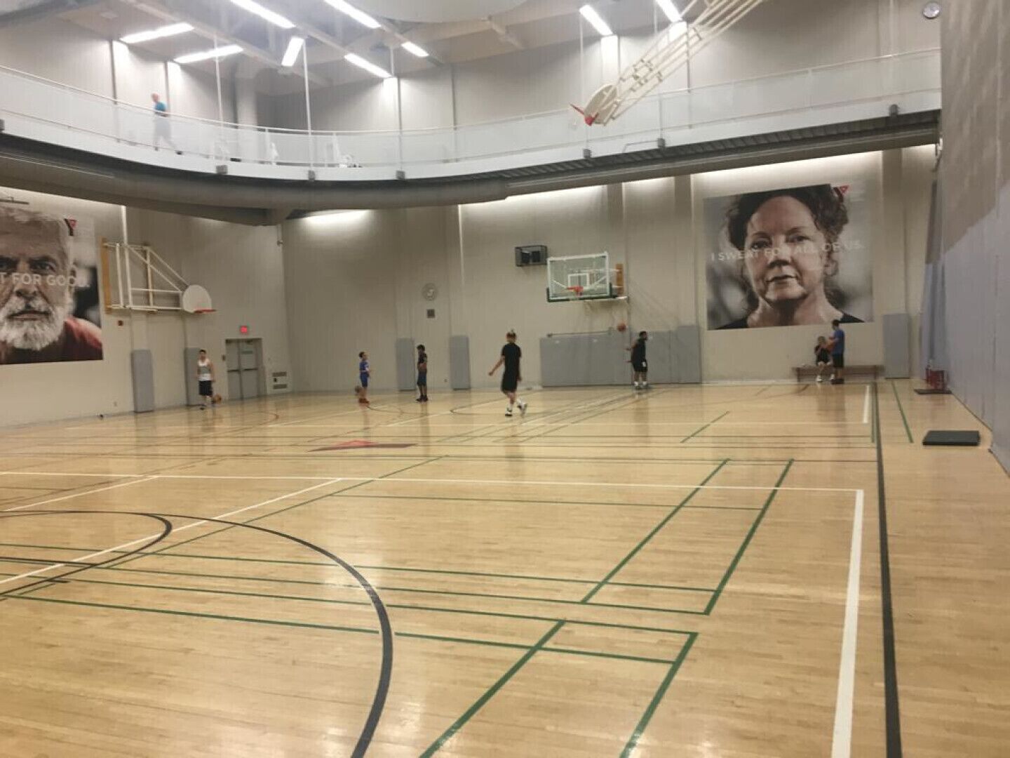 A large indoor basketball court with a high ceiling, a basketball hoop, and a mural on the wall.