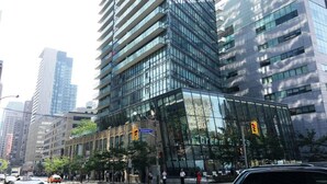 Un moderno edificio de gran altura con fachada de vidrio, situado en un entorno urbano rodeado de otros edificios altos.