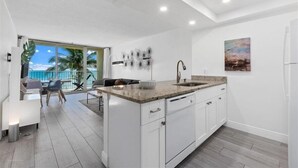 A modern kitchen with a large island, white cabinetry, and a view to a balcony.