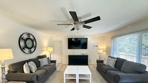 A living room with two sofas, a coffee table, a ceiling fan, a TV, and a wall clock. - Jonathan Livingston Seagull:  Dog friendly single story home. (Ocracoke)