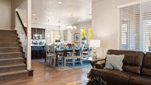 A spacious living area with a brown leather sofa, a dining table with chairs, a staircase, and a kitchen in the background. - PVZ 33|Steps to Pools *Misters* Pool/Mtn PatioView (Santa Clara)