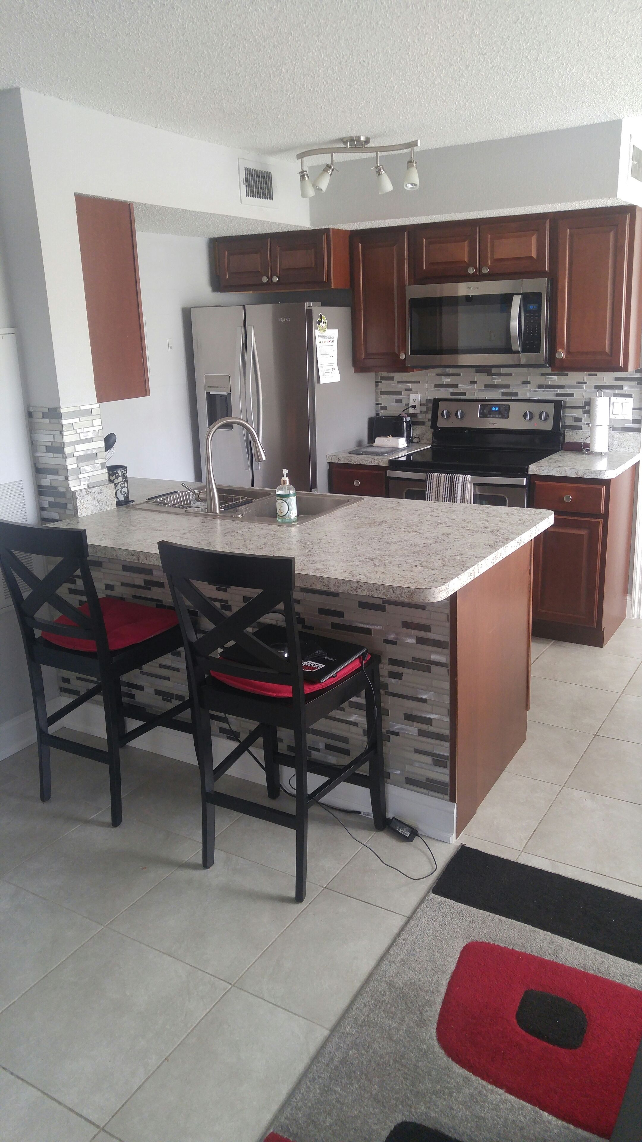 A modern kitchen with a central island, wooden cabinets, stainless steel appliances, and a tiled backsplash.