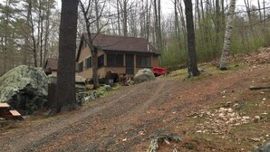 A cabin with a sloped roof, surrounded by trees and a dirt path. - Family Friendly Updated Waterfront Cottage (Leeds)