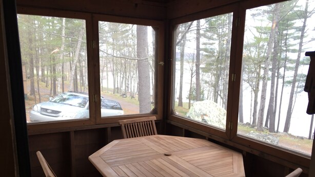A wooden table with six chairs in a corner with large windows. - Family Friendly Updated Waterfront Cottage (Leeds)