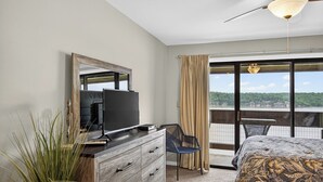 Habitación de hotel con una cama grande, un televisor en una cómoda de madera, un balcón con vistas y un ventilador de techo.