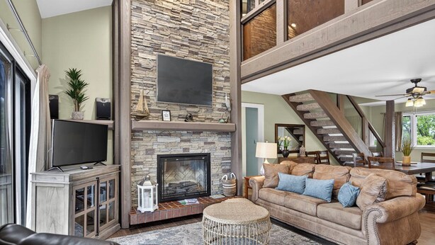 Una sala de estar con chimenea de piedra, televisor, sofá y una escalera.