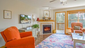 Un salon avec une cheminée, des fauteuils orange, un ventilateur de plafond et de grandes fenêtres.