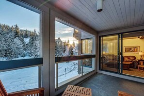 Huone, jossa on suuret ikkunat, joista avautuu näkymä lumiseen maisemaan ja kauempana sijaitsevaan rakennukseen.