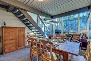 A dining area with a wooden table and chairs, a stone fireplace, and a staircase.