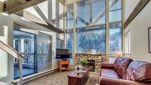 Una sala de estar con chimenea de piedra, ventanas amplias, un sofá de cuero y un televisor sobre un mueble.