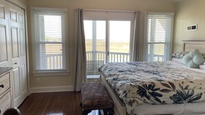 A bedroom with a bed, a bench, and a view of a balcony. - Folly Beach Riverfront Apt with dock, private boat ramp kayaks and bikes (Folly Beach)