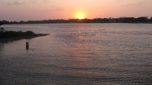 Un atardecer sobre un río tranquilo, con una línea de árboles a la distancia.
