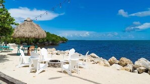 A beach setting with white chairs, a thatched-roof structure, and a string of lights. - NEW! Casa Azul - NO HIDDEN FEES! Golf Cart, 2 Kings, Pool, Beach, Tennis, Kayaks (Key Largo)