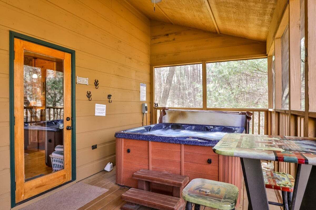 A wooden cabin with a hot tub, a table, and a door leading to a room.