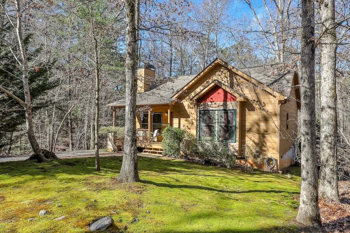 Une cabane avec une porte d’entrée rouge, entourée d’arbres et d’une pelouse bien entretenue.
