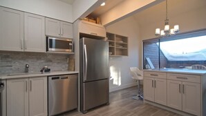 Una cocina moderna con electrodomésticos de acero inoxidable, armarios de tonos claros y vistas a través de una ventana.