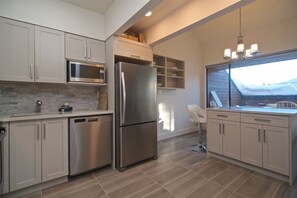 A modern kitchen with stainless steel appliances, light-colored cabinetry, and a view through a window. - Hearthstone Lodge - Hot tub - Village location - One bedroom loft (Whistler)