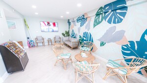 A room with wicker furniture, a TV, and a wall with tropical leaf patterns. - Steps from Pool & Beach, Oceanfront ground floor condo, Unit 106 (Satellite Beach)