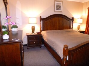 A neatly made bed with a wooden headboard, two bedside tables with lamps, a dresser with a mirror, and a framed picture on the wall. - Shorewalk rental By Owner/Condo 2bed/2bath/IMG Academy /Anna Maria Island (Bradenton)