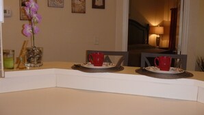 Un coin repas avec une table dressée pour deux personnes, agrémenté de tasses et d’assiettes rouges.