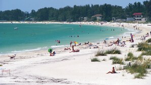 Une plage avec une eau turquoise et limpide, des gens qui se prélassent au soleil et des parasols.