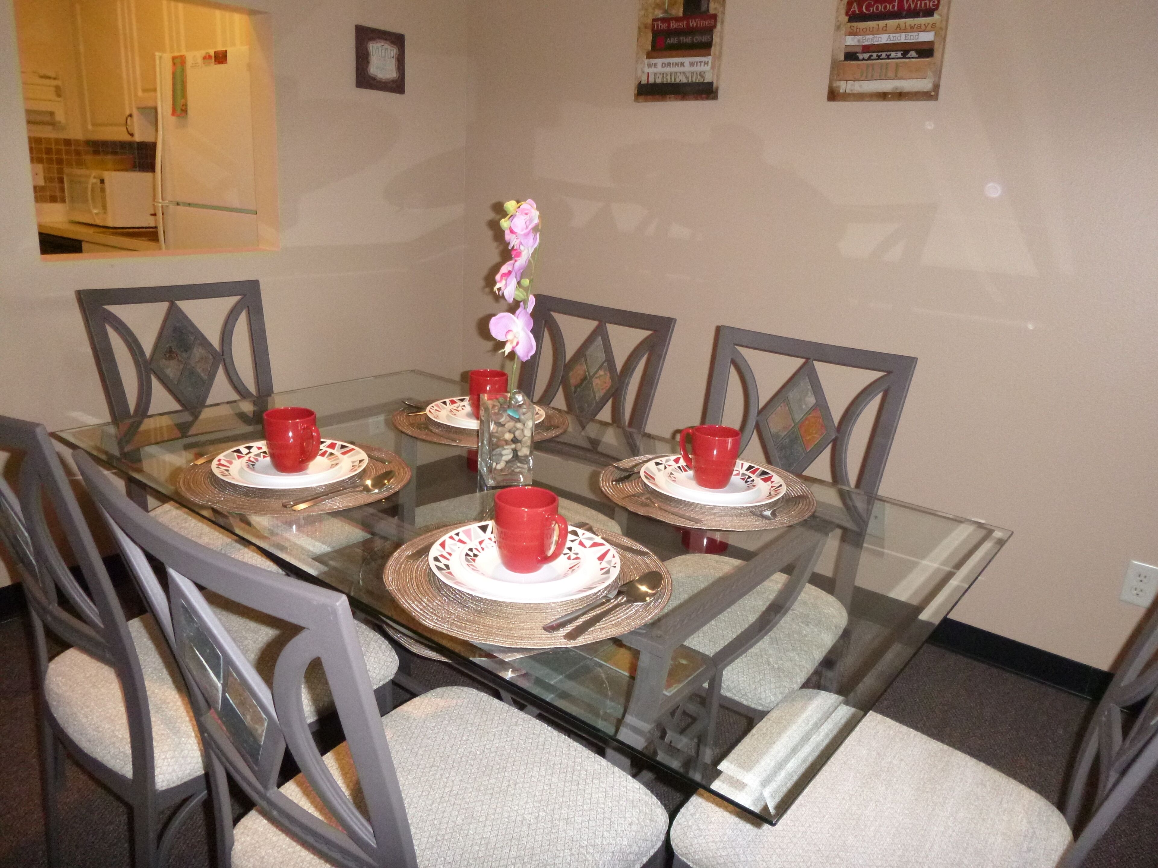 Uma mesa de jantar com quatro cadeiras, um vaso com flores e xícaras vermelhas sobre jogos americanos.