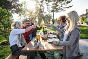 Un groupe de personnes trinquant autour d’une table en plein air, avec des boissons et de la nourriture, et entouré d’arbres.
