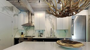 A modern kitchen with marble countertops, stainless steel appliances, and a unique antler chandelier. - 🌲Timberline D2H Deluxe 2-Bedroom ~Hot Tub~Pool~WiFi~Ski-in/out~Local Shuttle🌲 (Snowmass Village)
