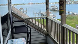 A covered balcony with a view of the water, a wooden deck, and a table with chairs. - Pirate's Quay 3 North: Incredible harbor views and sunsets. Docking. (Ocracoke)