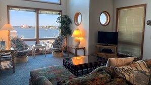 A living room with a large window overlooking a harbor, a television, and a cozy seating area. - Pirate's Quay 3 North: Incredible harbor views and sunsets. Docking. (Ocracoke)