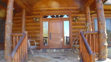 L’entrée d’un chalet en bois, avec un porche dallé de pierres, une porte en bois dotée de panneaux de verre et une cheminée en pierre.