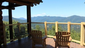 Eine Holzterrasse mit Adirondack-Stühlen mit Blick auf eine gebirgige Landschaft.