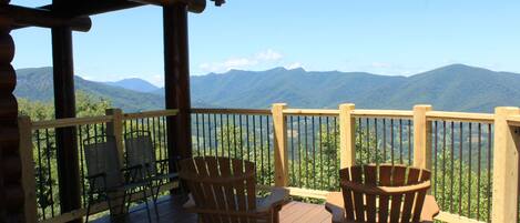 A wooden deck with Adirondack chairs overlooking a mountainous landscape.
