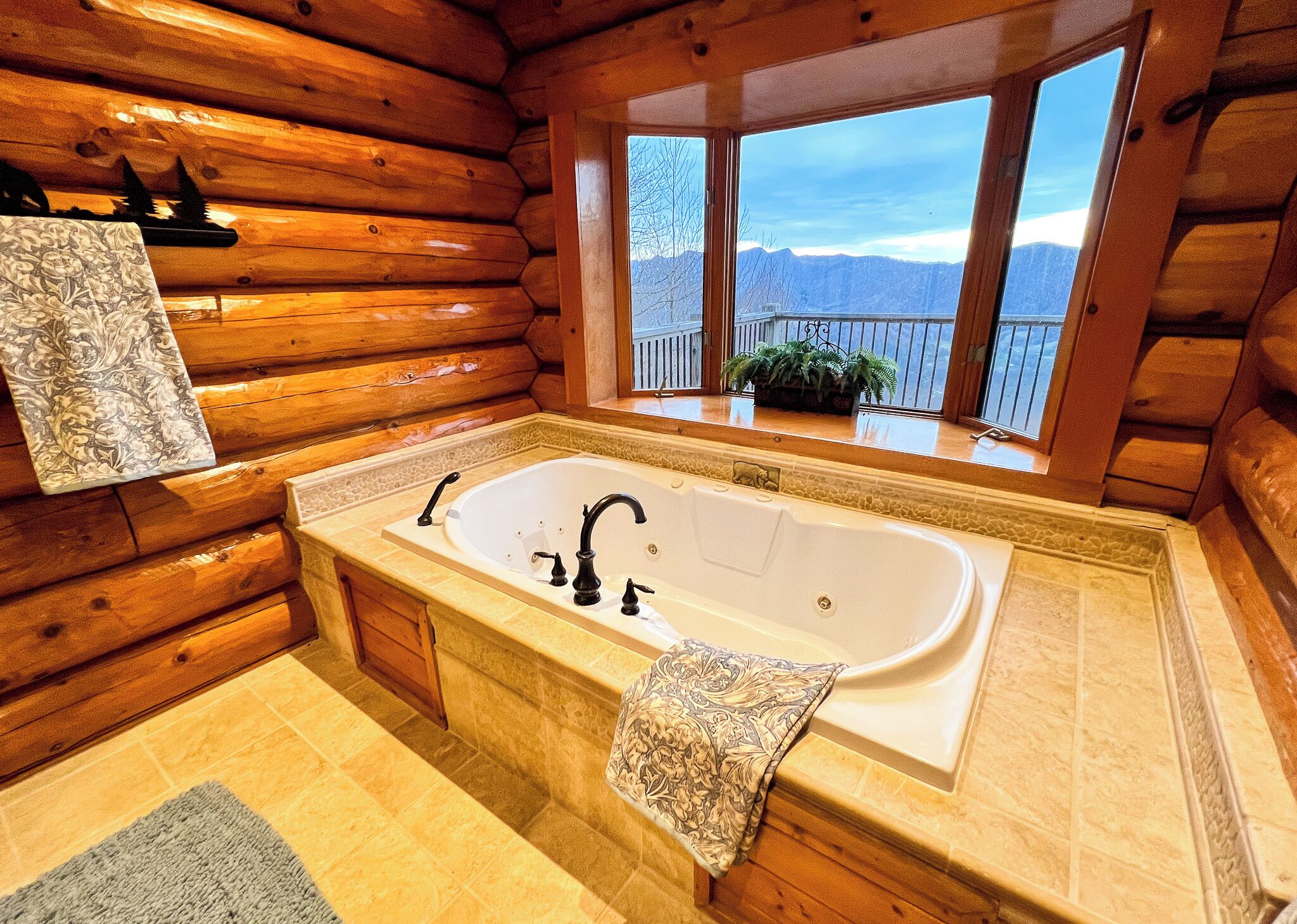 A log cabin bathroom with a large bathtub, wooden walls, and a view of mountains through a window.