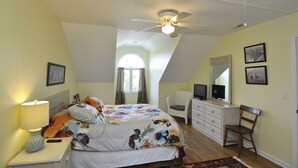 Een slaapkamer met een bed, nachtkastje, kapstok, stoel en plafondventilator.
