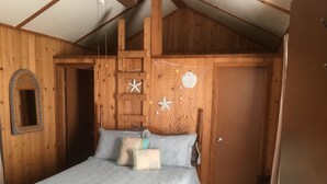 Camera da letto in una baita di legno, con un letto, un piccolo specchio e una decorazione a stella marina sul muro.