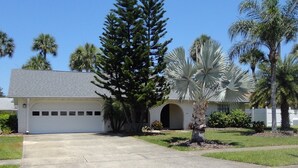 A single-story house with a garage, surrounded by palm trees and a well-maintained lawn. - Stay 5 Nights, Get 1 Night Free - 4 BR home in quiet setting close to everything (Port Orange)