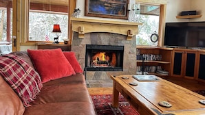A cozy living room with a fireplace, a sofa, a coffee table, and a bookshelf. - One of the Most Desirable Properties in the Winter Park / Fraser Valley (Tabernash)