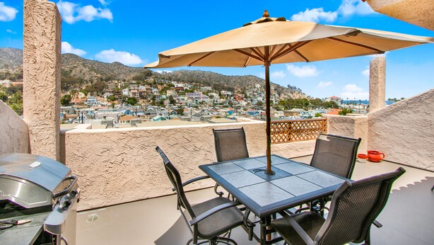 Eine Terrasse mit Tisch, Stühlen, Sonnenschirm und Grill.