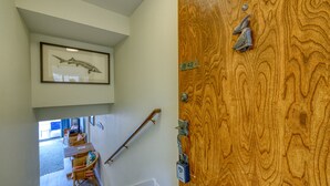 Eine Holztür mit einer Messing-Klopfer, ein gerahmtes Bild von einem Fisch an der Wand und eine Treppe, die in einen Essbereich führt.