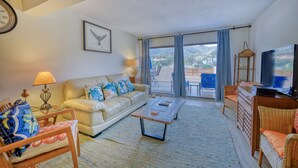 Ein Wohnzimmer mit einer Couch, einem Couchtisch und Korbmöbeln. Ein Fernseher und eine Lampe stehen auf einem Beistelltisch.