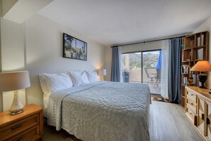 Ein Schlafzimmer mit Bett, Nachttisch, Lampe und Blick ins Freie durch eine Schiebetür.